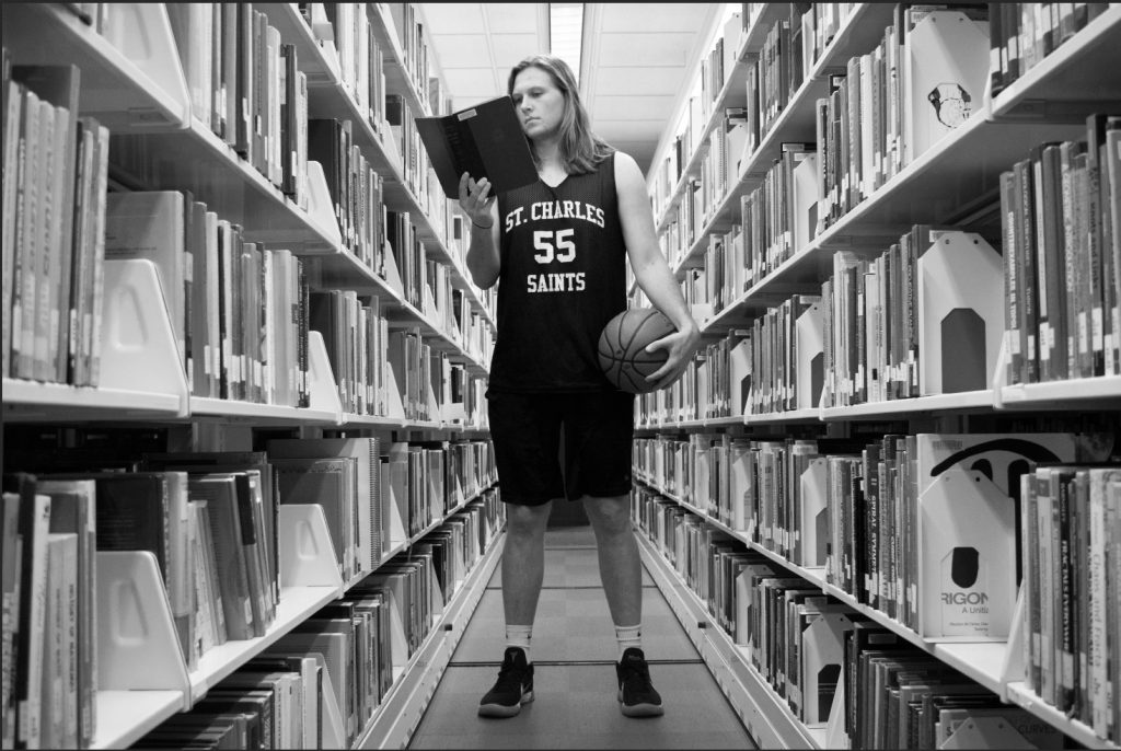 Basketball player dressed for a game, reading a book in the library